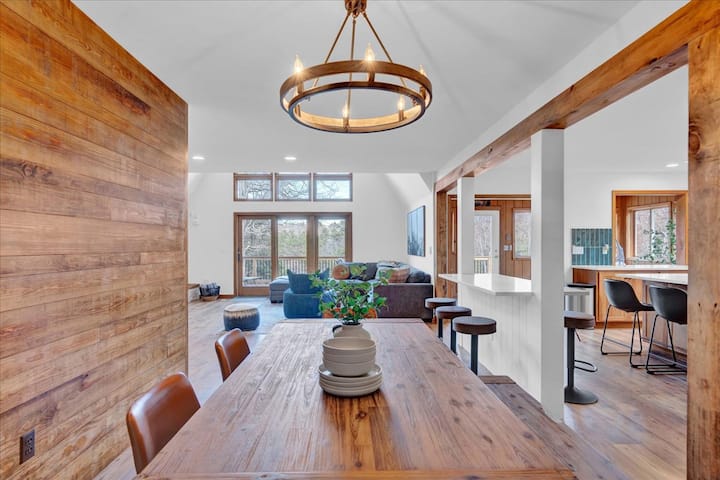 Wooden dining table with a circular chandelier and a view into Powderhorn Cove’s living room
